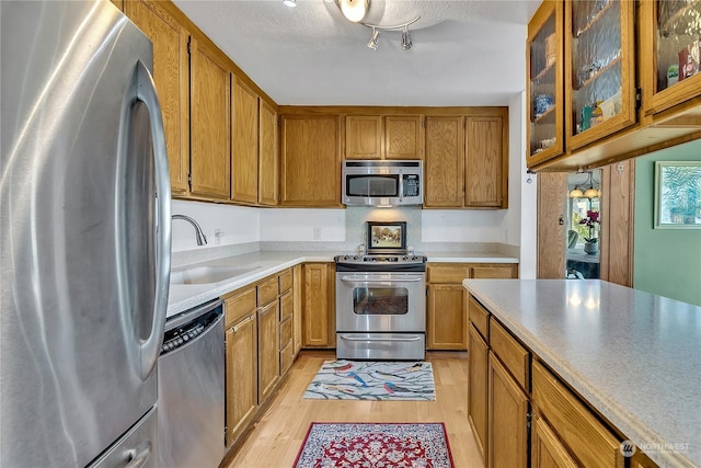 kitchen with appliances with stainless steel finishes, sink, a textured ceiling, and light wood-type flooring