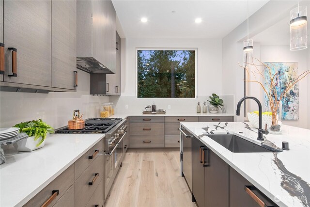 kitchen featuring stainless steel appliances, pendant lighting, sink, light hardwood / wood-style floors, and wall chimney exhaust hood