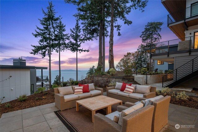 patio terrace at dusk with a balcony, outdoor lounge area, and a water view