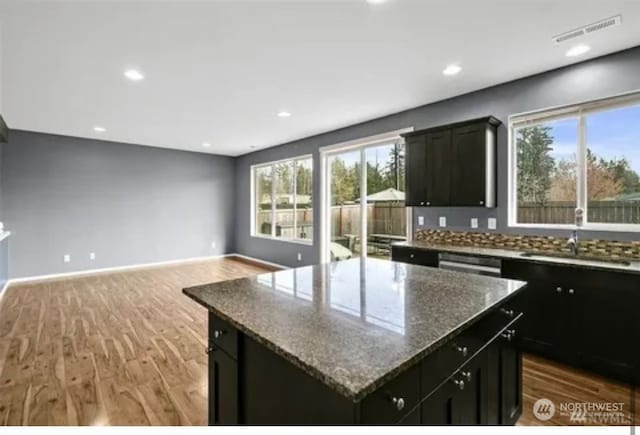 kitchen with light stone counters, sink, backsplash, hardwood / wood-style flooring, and a center island