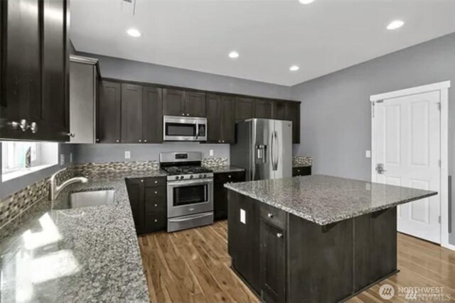 kitchen featuring wood-type flooring, a center island, sink, appliances with stainless steel finishes, and light stone countertops