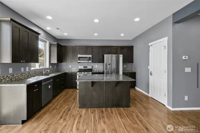 kitchen with stone countertops, dark brown cabinets, a kitchen island, appliances with stainless steel finishes, and light hardwood / wood-style floors