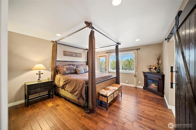 bedroom featuring a barn door, wood finished floors, a glass covered fireplace, and baseboards