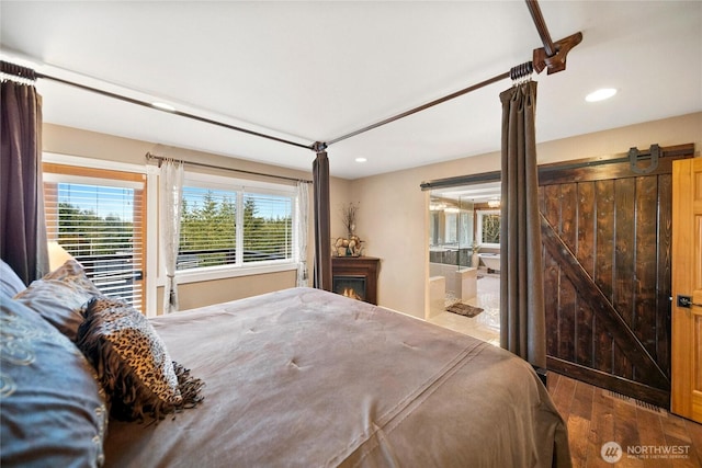 bedroom featuring ensuite bath, a barn door, wood finished floors, and recessed lighting