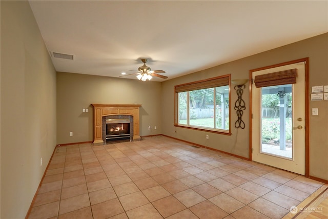 unfurnished living room featuring ceiling fan, a fireplace, light tile patterned floors, and plenty of natural light