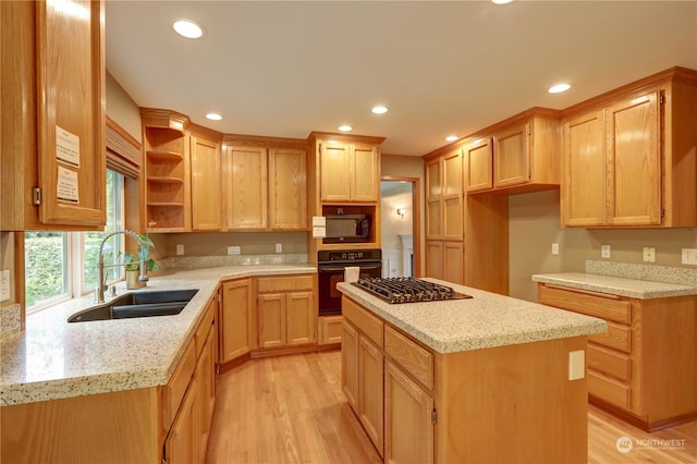 kitchen featuring a kitchen island, black oven, sink, light stone countertops, and light wood-type flooring