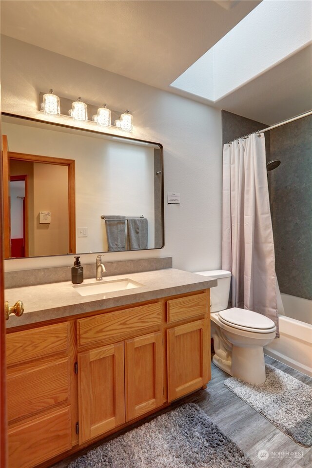 full bathroom featuring wood-type flooring, toilet, shower / bath combo, a skylight, and vanity