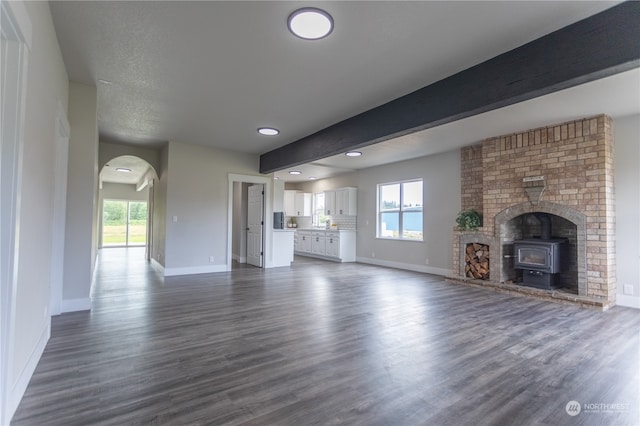 unfurnished living room with beam ceiling, a wood stove, brick wall, and dark hardwood / wood-style floors