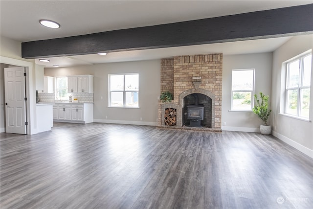 unfurnished living room featuring plenty of natural light, beam ceiling, hardwood / wood-style flooring, and a brick fireplace