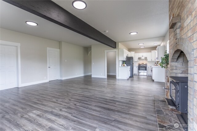 unfurnished living room featuring beamed ceiling, a stone fireplace, and dark hardwood / wood-style flooring