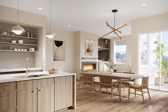 kitchen featuring hanging light fixtures, light wood-type flooring, a tile fireplace, sink, and light stone counters