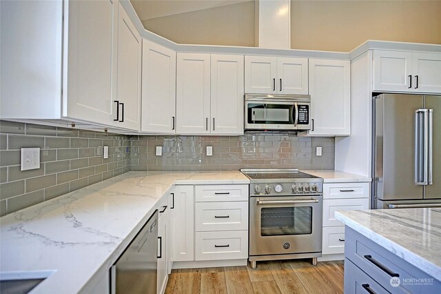 kitchen with light wood-type flooring, decorative backsplash, light stone countertops, and premium appliances