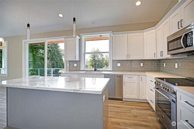 kitchen featuring light wood-type flooring, decorative light fixtures, appliances with stainless steel finishes, and decorative backsplash