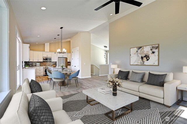 living room featuring high vaulted ceiling, ceiling fan with notable chandelier, and light wood-type flooring