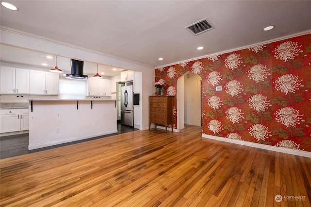 kitchen with arched walkways, visible vents, freestanding refrigerator, range hood, and wallpapered walls