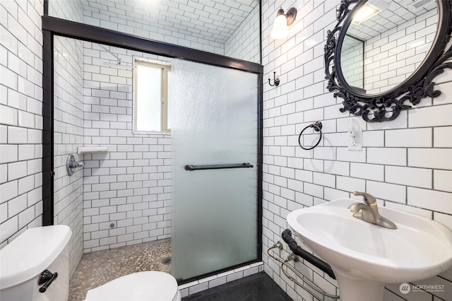 bathroom featuring toilet, a stall shower, tile walls, and a sink