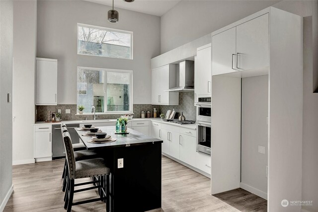 kitchen with pendant lighting, wall chimney range hood, white cabinetry, stainless steel appliances, and a kitchen island