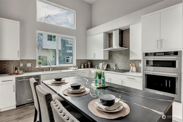 kitchen with wall chimney exhaust hood, sink, tasteful backsplash, appliances with stainless steel finishes, and white cabinets