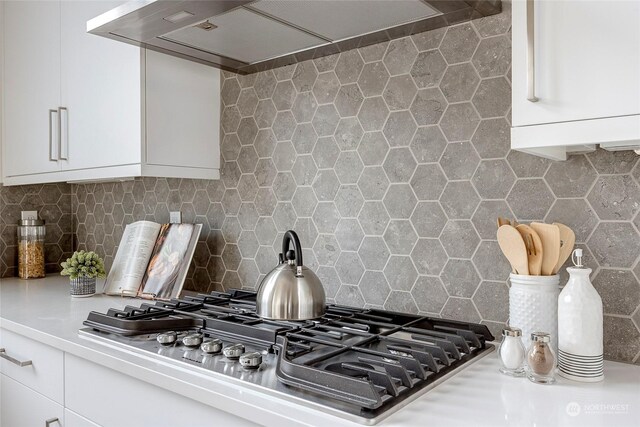 kitchen featuring tasteful backsplash, wall chimney exhaust hood, stainless steel gas cooktop, and white cabinets