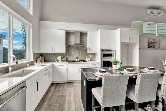 kitchen with sink, a breakfast bar, wall chimney exhaust hood, and appliances with stainless steel finishes