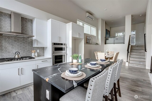 kitchen featuring stainless steel appliances, a kitchen island, white cabinets, and wall chimney exhaust hood