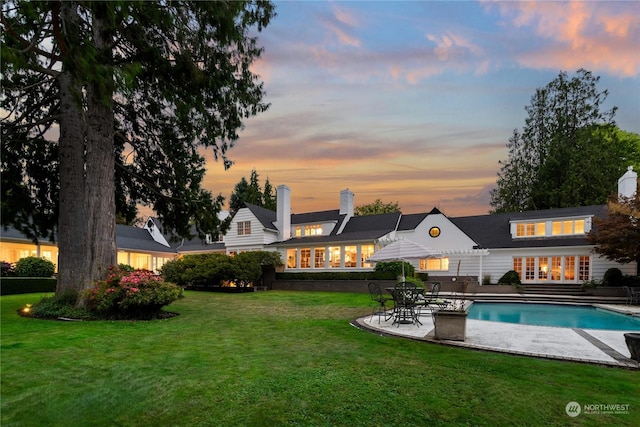 back of house featuring a yard, an outdoor pool, a patio, and a chimney