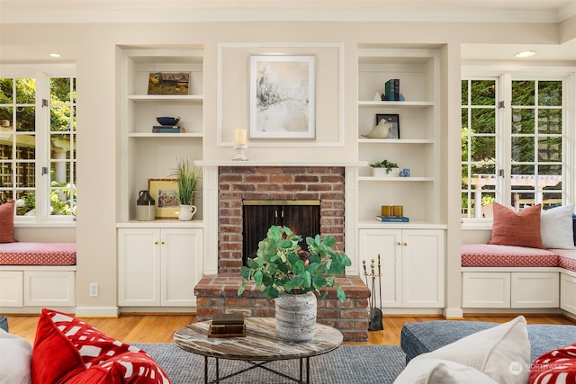 living room with built in shelves, light wood-type flooring, crown molding, and a brick fireplace