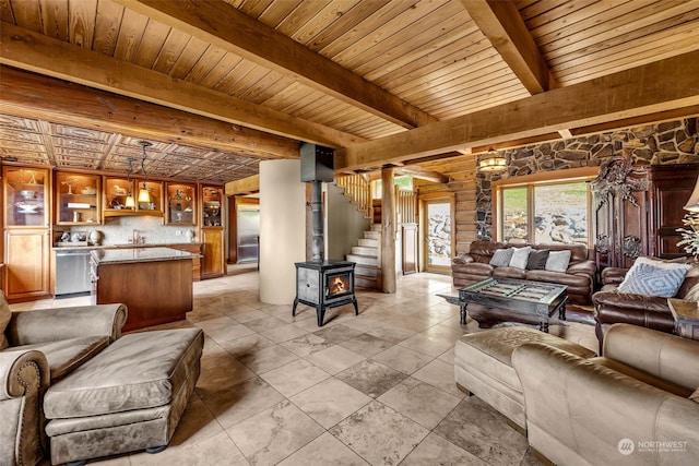 living room featuring a wood stove, beamed ceiling, wooden ceiling, and sink