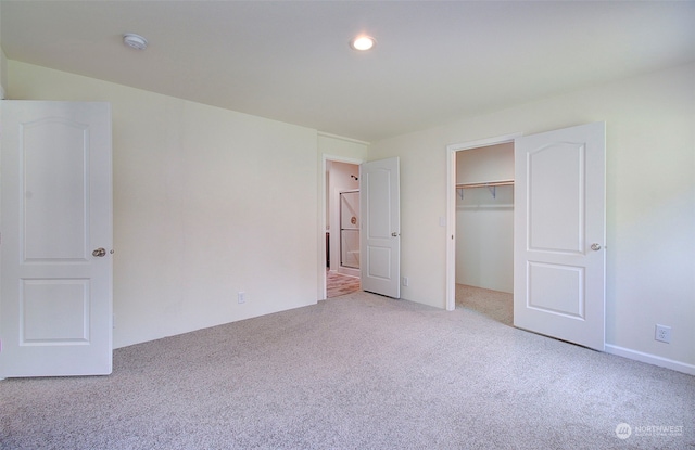 unfurnished bedroom featuring a walk in closet, a closet, and light colored carpet