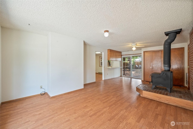 unfurnished living room with a ceiling fan, a wood stove, light wood finished floors, and a textured ceiling