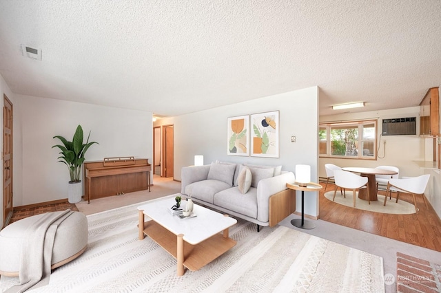 living area featuring visible vents, wood finished floors, a wall unit AC, and a textured ceiling