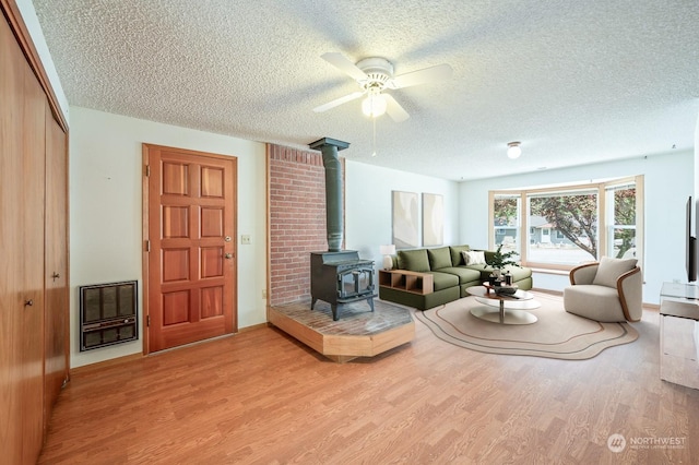 living room with a wood stove, ceiling fan, wood finished floors, and a textured ceiling