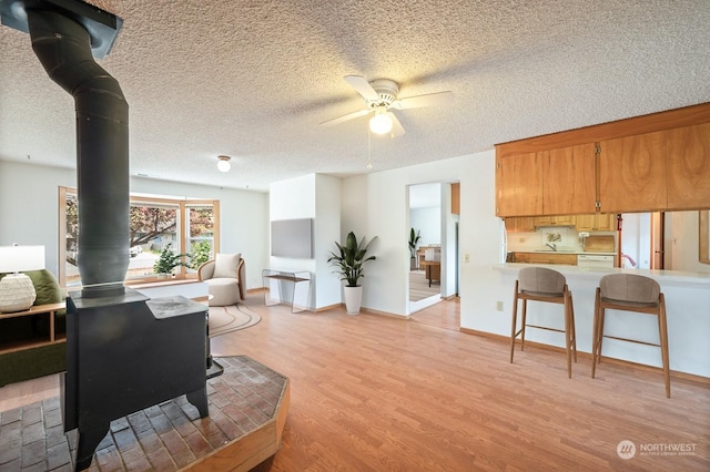 living room with a wood stove, light wood-style flooring, a textured ceiling, and a ceiling fan