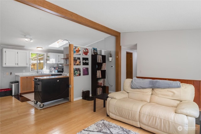 living room featuring vaulted ceiling with skylight, light wood-style flooring, and a textured ceiling