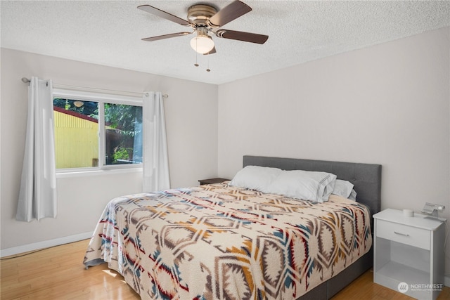 bedroom featuring baseboards, ceiling fan, light wood-style flooring, and a textured ceiling