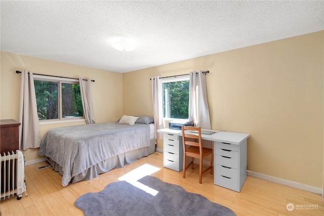 bedroom featuring light wood finished floors, radiator heating unit, and baseboards