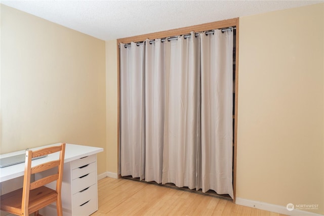 unfurnished office featuring light wood-style floors, a textured ceiling, and baseboards