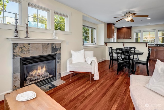 living room featuring dark wood-type flooring, ceiling fan, and a tile fireplace