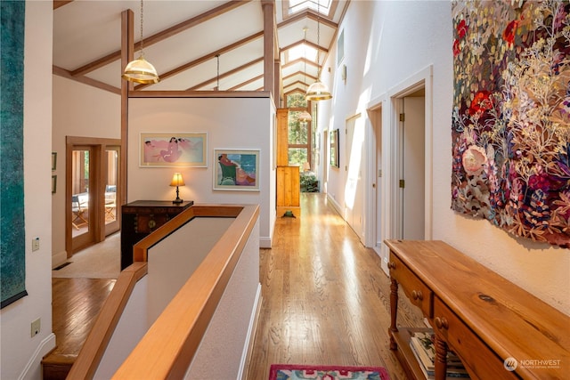 hallway with light wood-style floors, high vaulted ceiling, beamed ceiling, and an upstairs landing