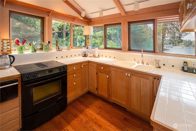 kitchen with brown cabinetry, black range with electric cooktop, a sink, and tile counters