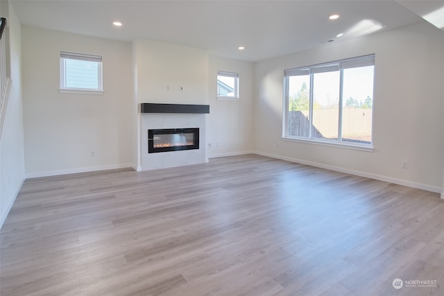 unfurnished living room with a tiled fireplace and light hardwood / wood-style flooring