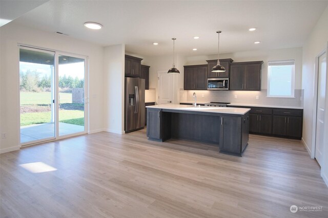 kitchen featuring backsplash, stainless steel appliances, a kitchen island with sink, and light hardwood / wood-style flooring