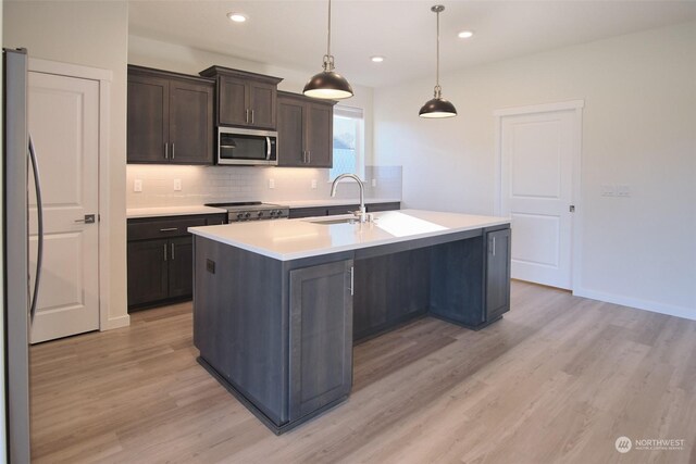 kitchen with stainless steel appliances, sink, an island with sink, light wood-type flooring, and pendant lighting