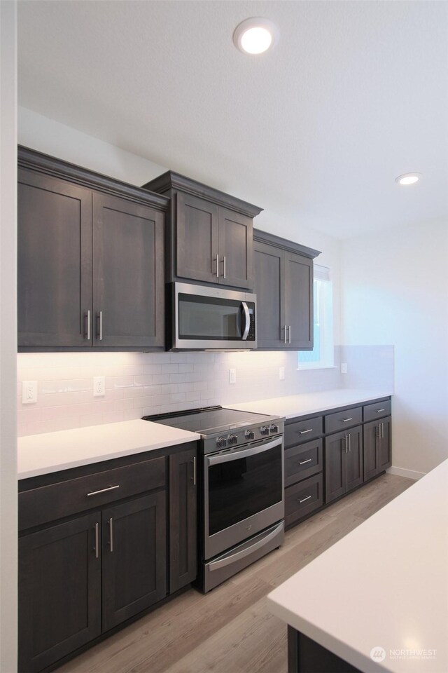 kitchen featuring appliances with stainless steel finishes, light hardwood / wood-style flooring, dark brown cabinets, and backsplash