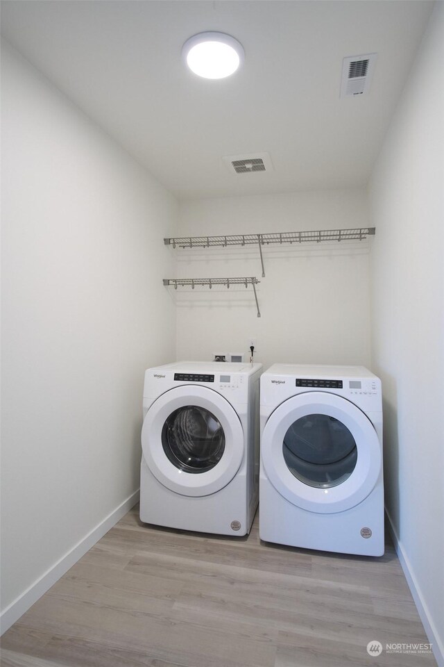 washroom with washing machine and clothes dryer and light hardwood / wood-style flooring