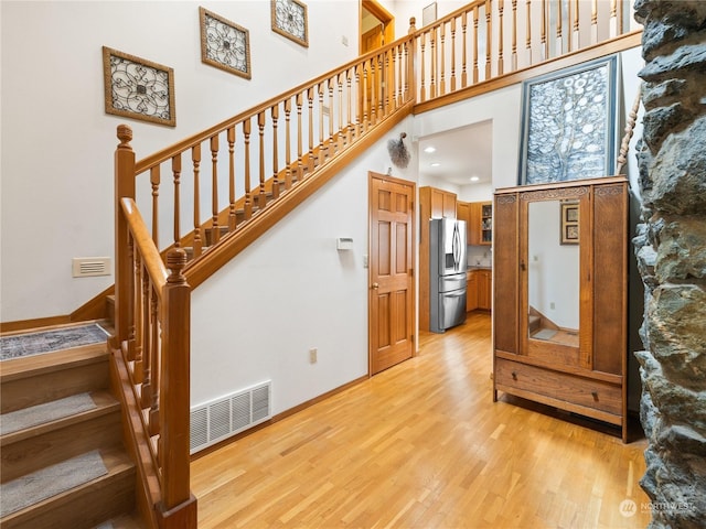 stairs with a high ceiling, wood finished floors, visible vents, and baseboards