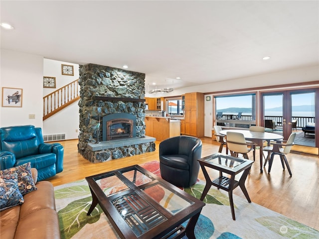 living room with light wood-style floors, stairs, visible vents, and a stone fireplace