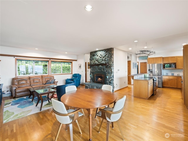 dining room with light wood finished floors, recessed lighting, and a stone fireplace