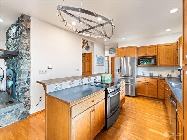 kitchen featuring dark countertops, appliances with stainless steel finishes, brown cabinetry, light wood-style floors, and a kitchen island