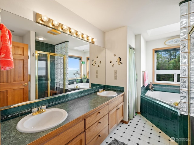 full bath featuring a skylight, a garden tub, double vanity, a sink, and a shower stall